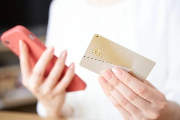 女性が赤いスマートフォンと金色のクレジットカードを手に持ち、オンラインでの支払い準備をしている様子