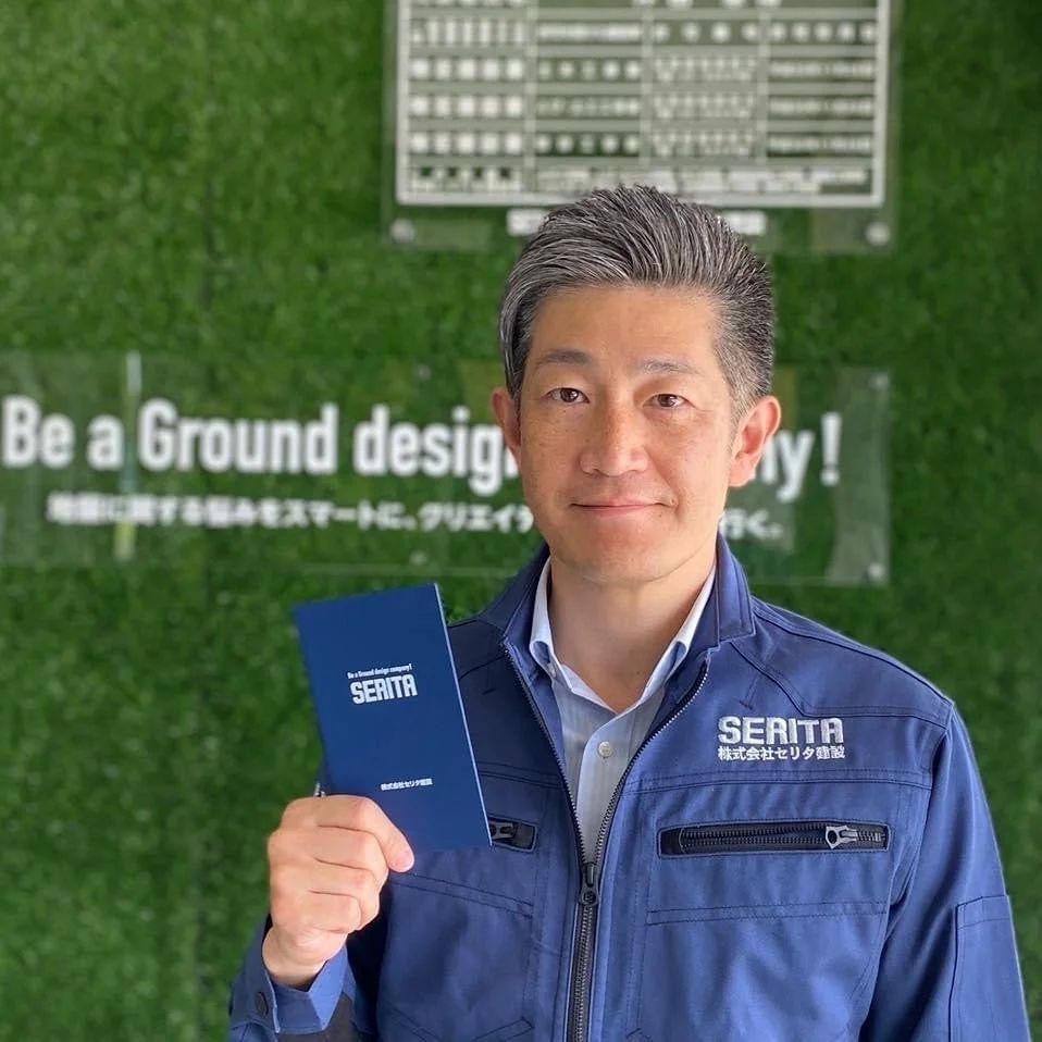 青い作業服を着て笑顔で立つ男性